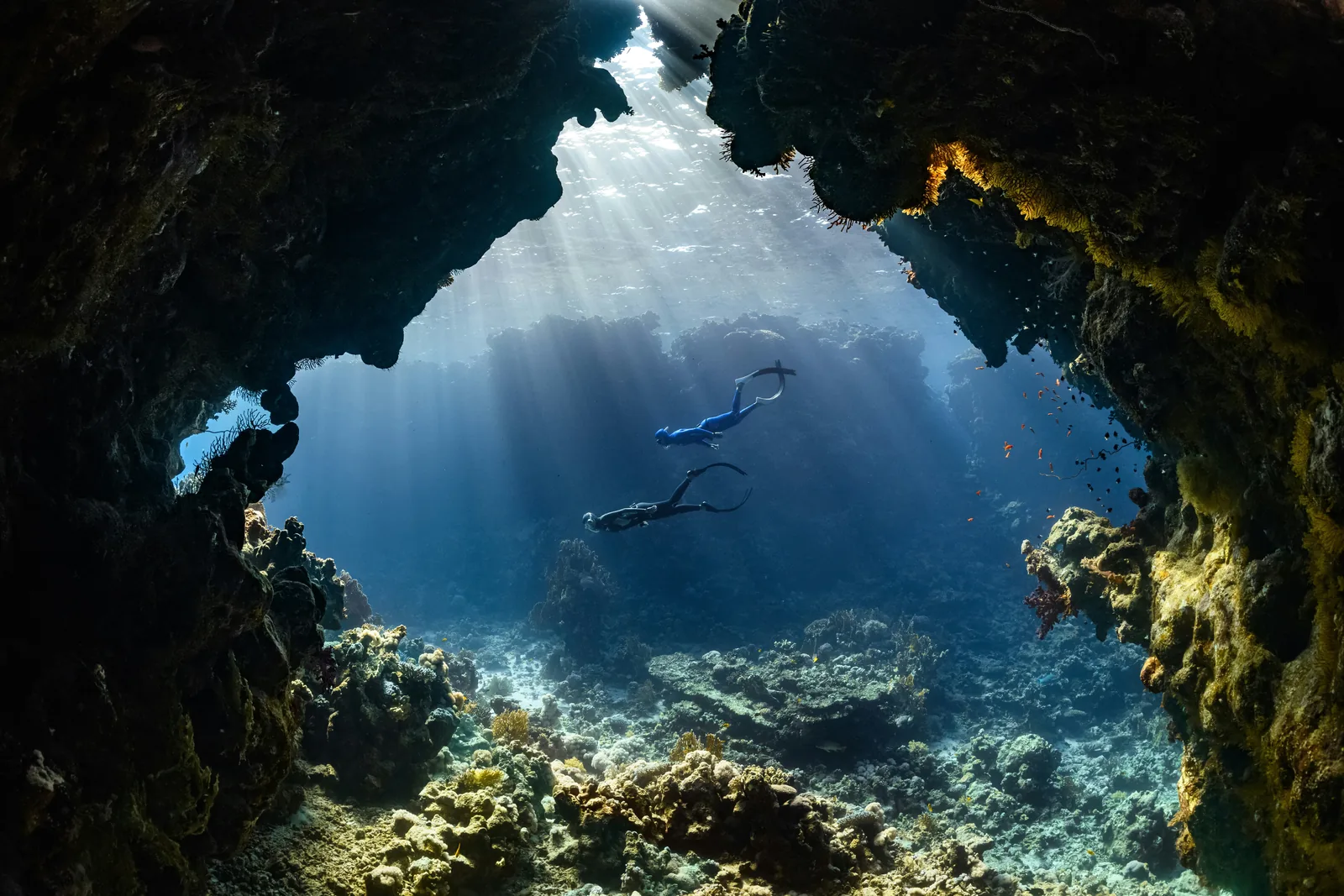 Dos buceadores descienden por la boca de una cueva submarina mientras la luz entra desde arriba