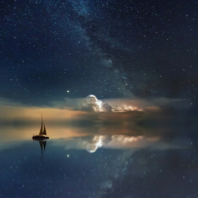 Un velero navegando en calma bajo la Vía Láctea, reflejado en el agua